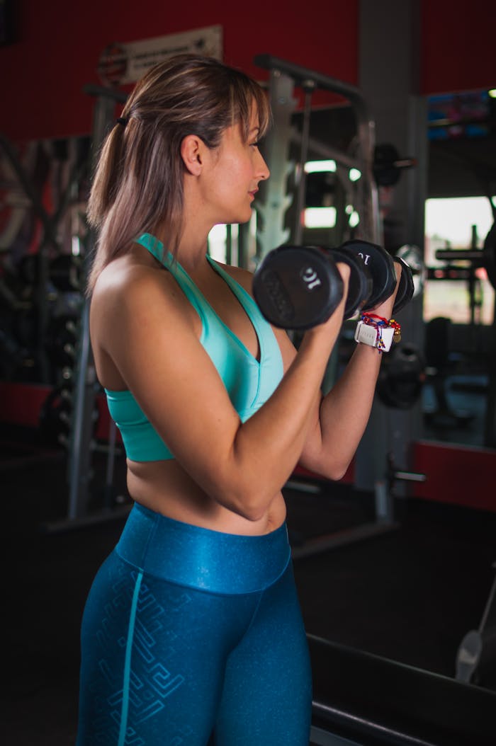 A fit woman lifting dumbbells in a gym, showcasing strength and focus during her workout.
